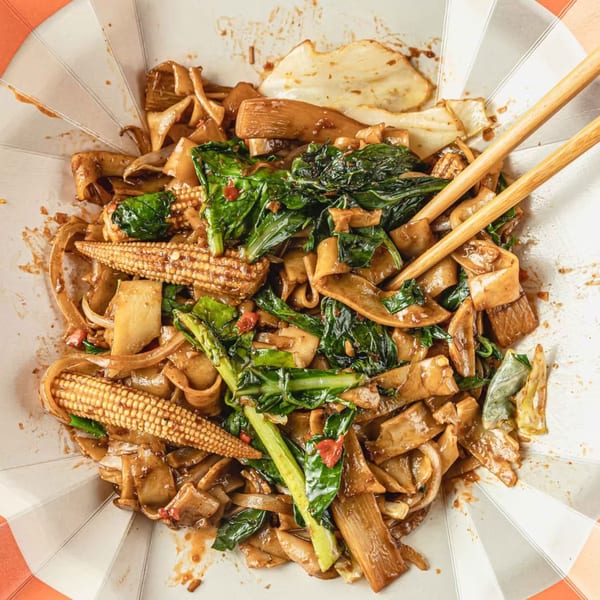 Close-up of Thai Pad See Ew noodles with baby corn, green vegetables, and chopsticks in a bowl.