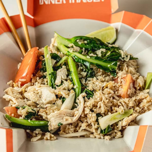 Thai fried rice with chicken, green vegetables, tomatoes, and a lime wedge in a takeout container.