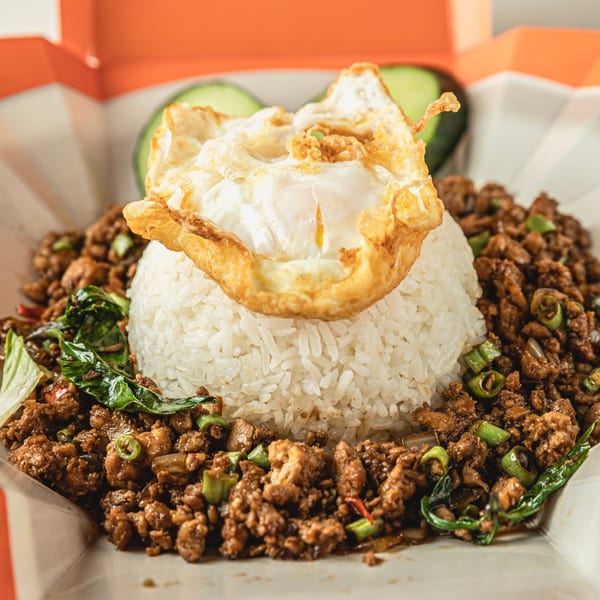 Thai basil chicken with rice and a fried egg, served in a takeout container.