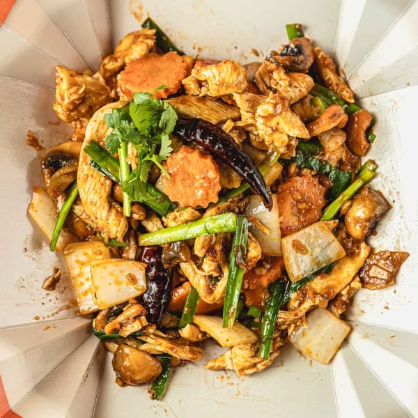 Thai stir-fried chicken with vegetables, mushrooms, and chili in a takeout container.