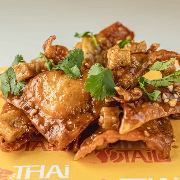 Thai crispy wontons with sweet chili sauce, peanuts, and cilantro on a yellow Thai Tail branded surface.