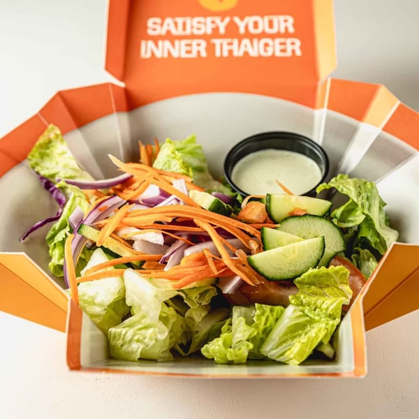 Fresh Thai salad with lettuce, carrots, cucumbers, red onions, and dressing in an orange box.